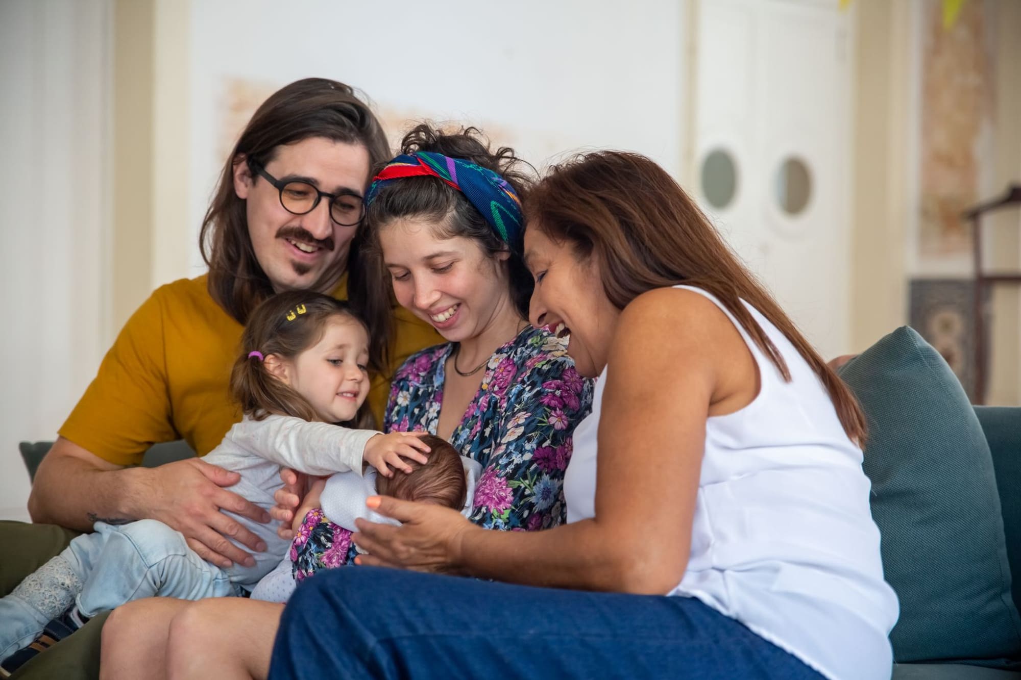 משפחה משלושה דורות יושבת יחד על ספה ומביטה בתינוק